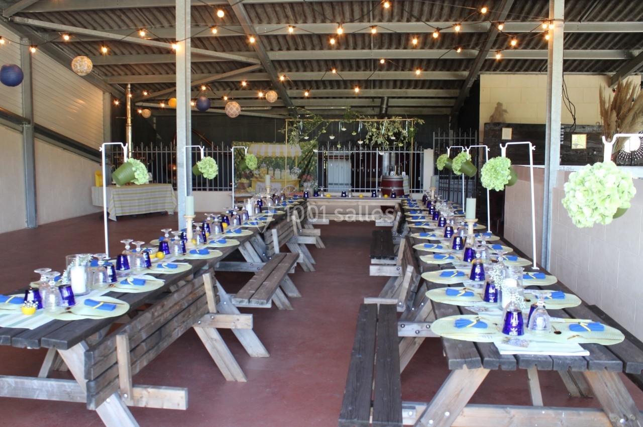 Tables en bois alignées dans une salle décorée avec des guirlandes lumineuses et des éléments floraux suspendus.