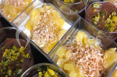 Assortiment de verrines sucrées avec mousse, caramel, mangue et chantilly, disposées sur un plateau noir.