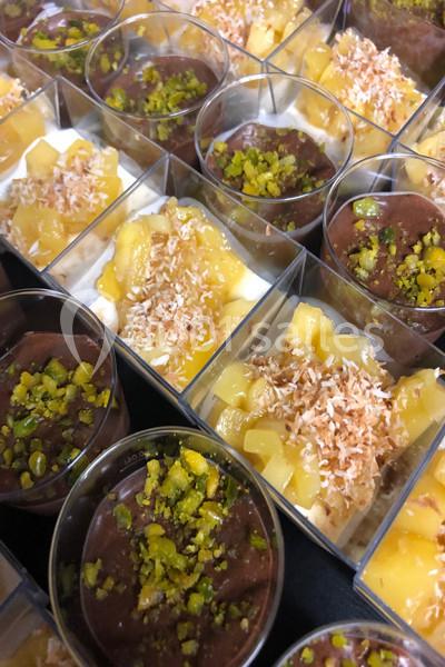 Desserts en verrines garnis de morceaux de mangue, noix de coco râpée et éclats de pistache.