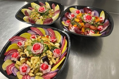 Trois salades colorées présentées dans des bols noirs, composées de légumes variés et décorées de radis sculptés.