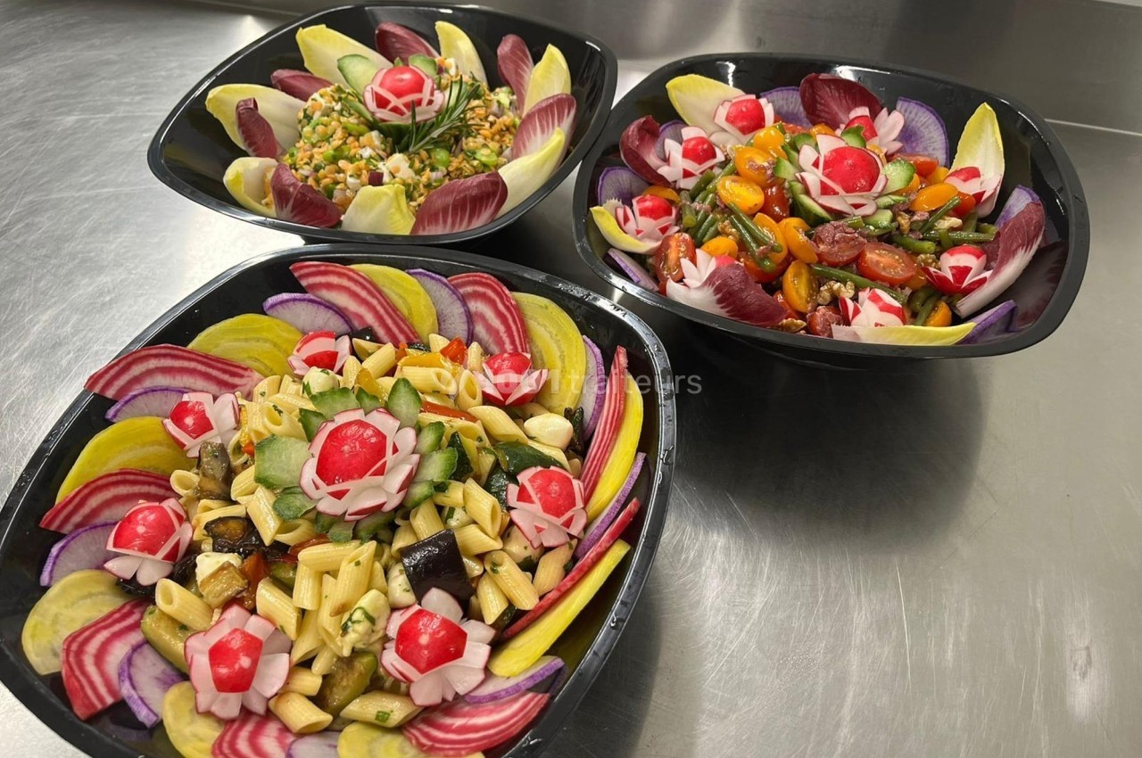 Trois salades colorées présentées dans des bols noirs, composées de légumes variés et décorées de radis sculptés.