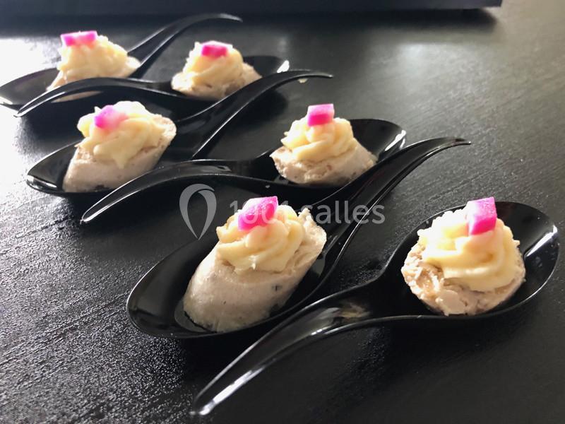 Cuillères noires contenant des bouchées garnies de mousse blanche et décorées de dés roses, disposées sur une table sombre.