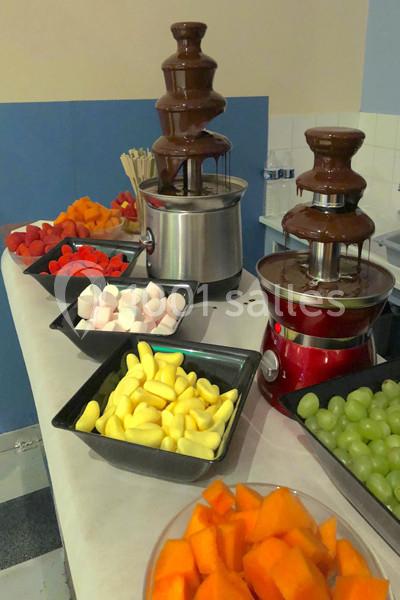 Fontaines de chocolat entourées de fruits frais, guimauves et brochettes sur une table de buffet.
