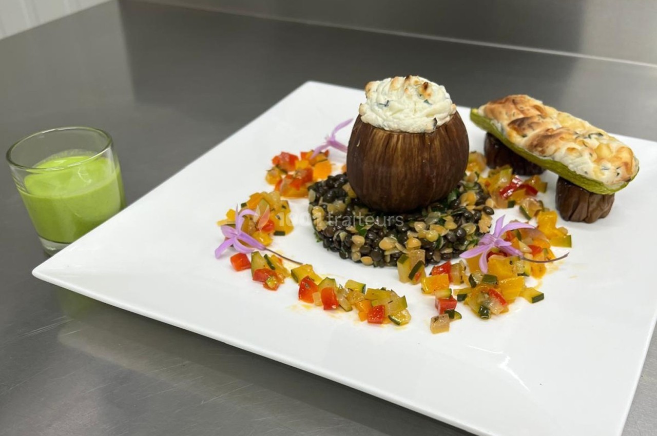 Assiette gastronomique avec aubergine farcie, lentilles, légumes colorés, pain garni et verrine de soupe verte.