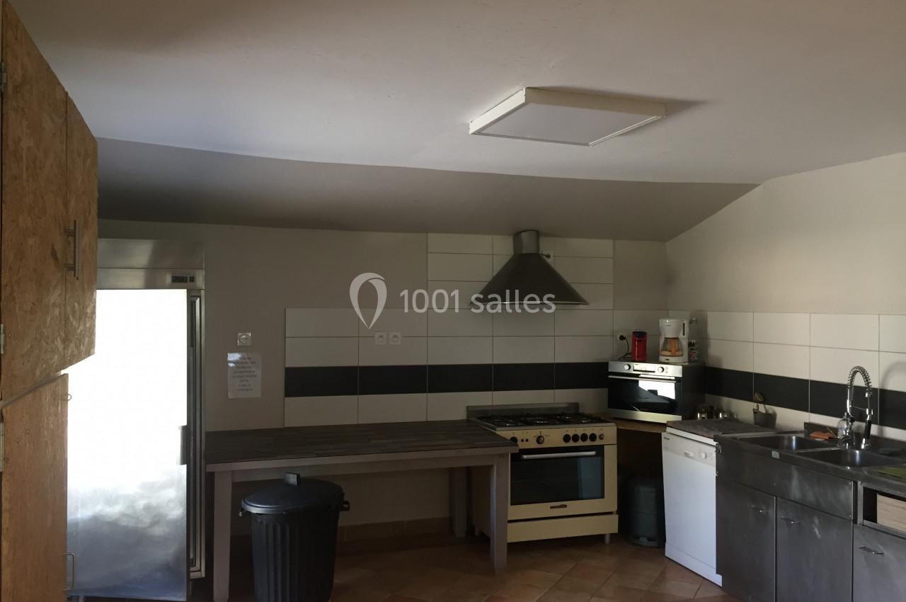 Cuisine équipée avec évier, cuisinière, hotte, réfrigérateur, plan de travail et poubelle dans un espace lumineux.