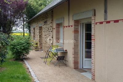Chaise en bois marquée ’Gîte de la Barre’ dans un jardin verdoyant près d'une maison en pierre et crépi.