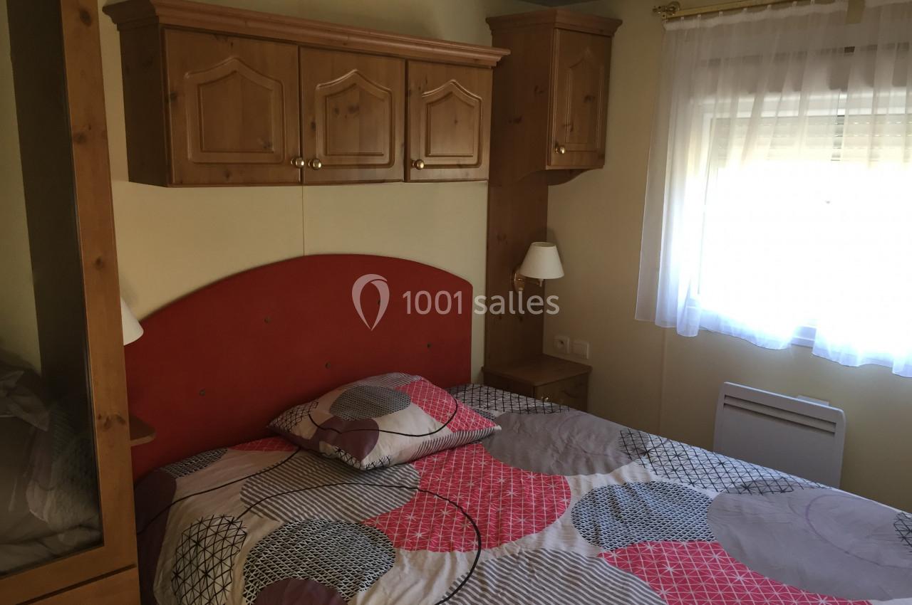 Chambre avec lit double, tête de lit rouge, meubles en bois, fenêtre avec rideau blanc laissant entrer la lumière.