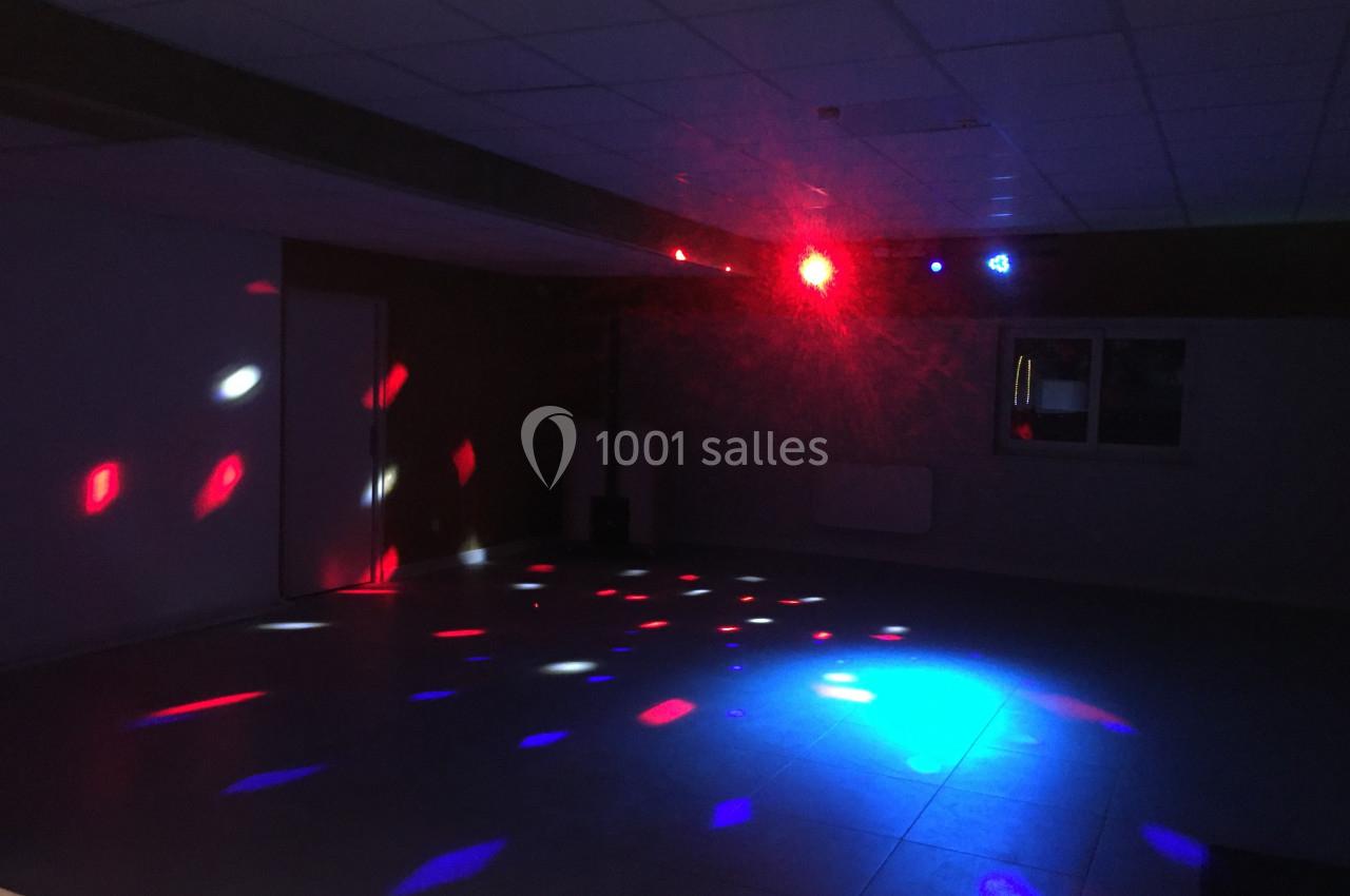 Salle sombre avec des lumières colorées projetées au sol et au mur, créant une ambiance festive.