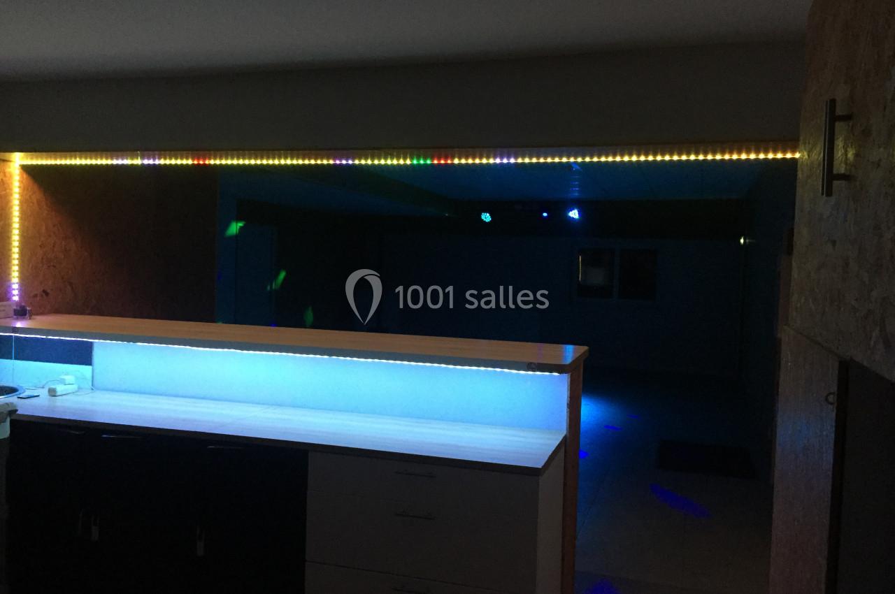 Plan de travail éclairé par des LED colorées dans une pièce sombre avec un mur en bois et un espace ouvert en arrière-plan.