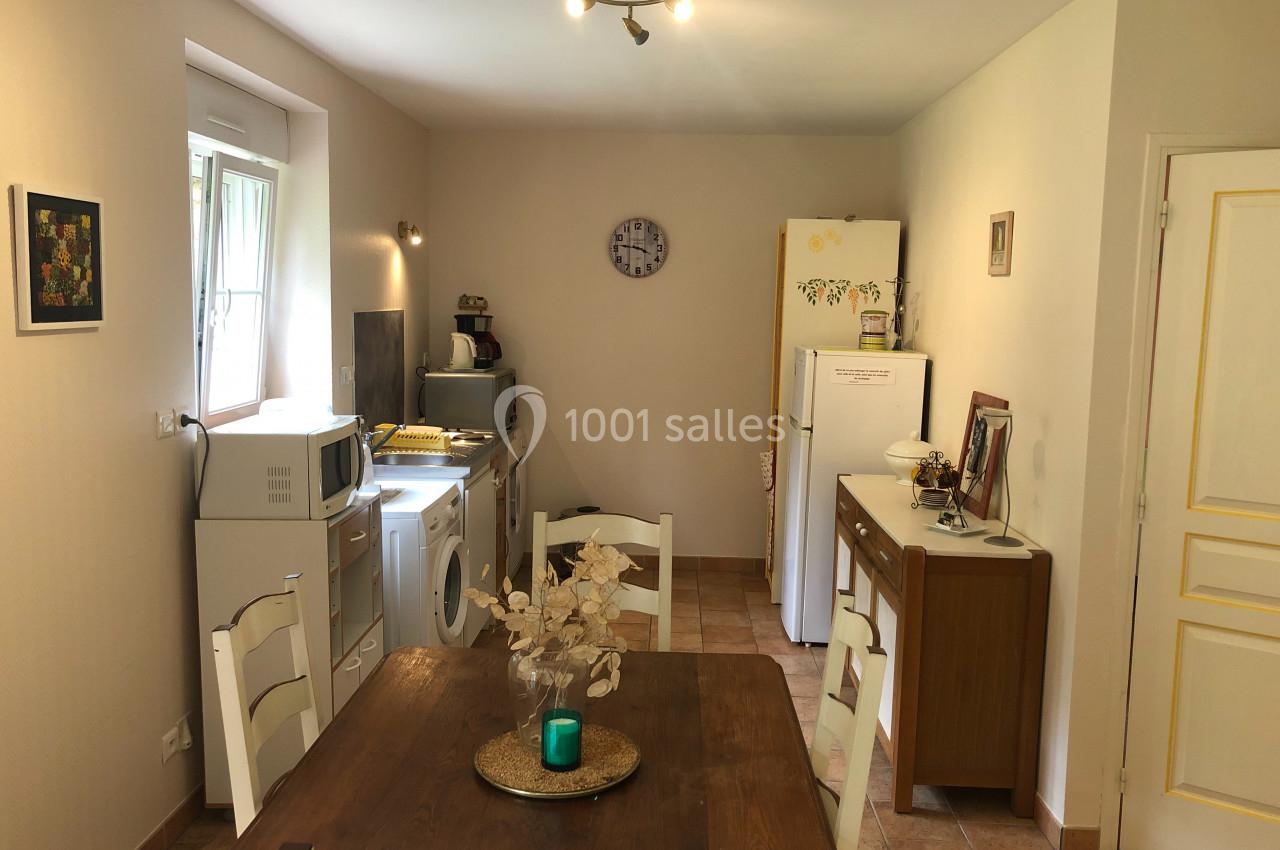 Cuisine lumineuse avec table en bois, électroménagers, réfrigérateur, et décoration murale dans un intérieur sobre.