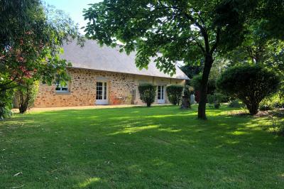 Chaise en bois marquée ’Gîte de la Barre’ dans un jardin verdoyant près d'une maison en pierre et crépi.