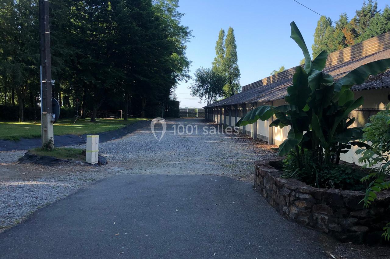 Chemin asphalté bordé de bâtiments à droite et d'arbres à gauche, sous un ciel dégagé.