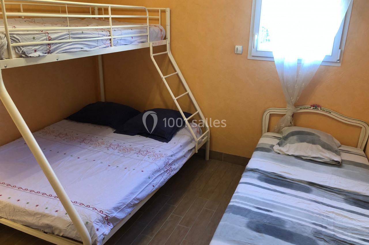 Chambre avec lits superposés et lit simple, draps clairs, murs orange et fenêtre avec rideau blanc.