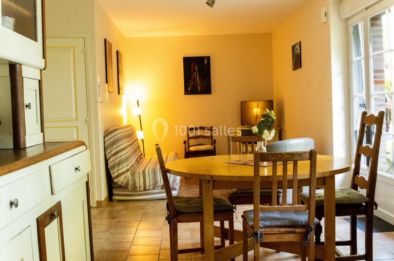 Salle à manger lumineuse avec table en bois, chaises, canapé, lampadaire et vue sur une porte-fenêtre donnant sur l…