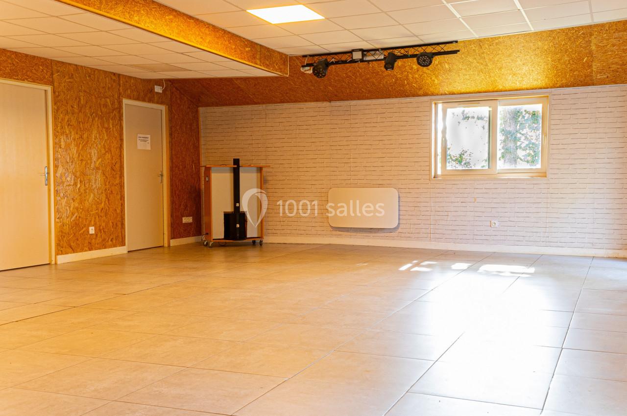 Salle vide avec sol en carrelage, murs en bois et briques blanches, fenêtre laissant entrer la lumière naturelle.
