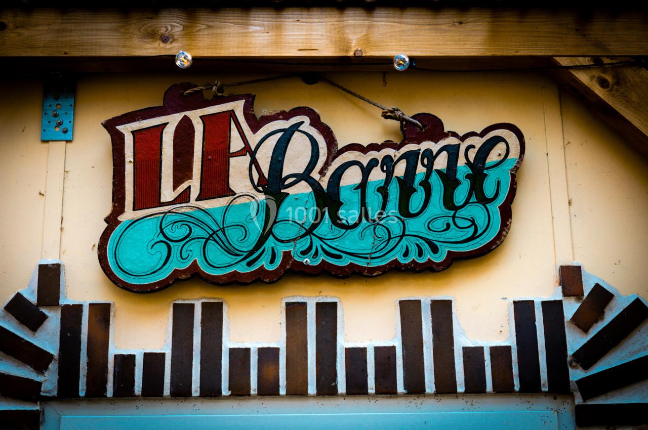 Enseigne en bois colorée avec l'inscription ’Le Barri’, suspendue sur une façade ornée de motifs géométriques.