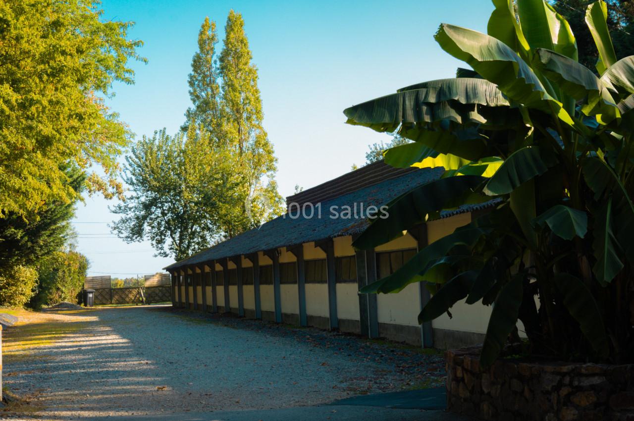 Allée bordée de végétation menant à un bâtiment avec un toit en tuiles, sous un ciel dégagé.
