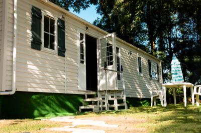 Chaise en bois marquée ’Gîte de la Barre’ dans un jardin verdoyant près d'une maison en pierre et crépi.
