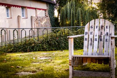 Chaise en bois marquée ’Gîte de la Barre’ dans un jardin verdoyant près d'une maison en pierre et crépi.