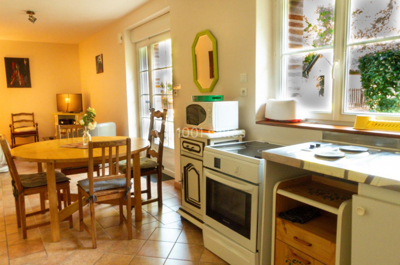 Cuisine lumineuse avec table ronde en bois, chaises, four, micro-ondes et fenêtre donnant sur un jardin.