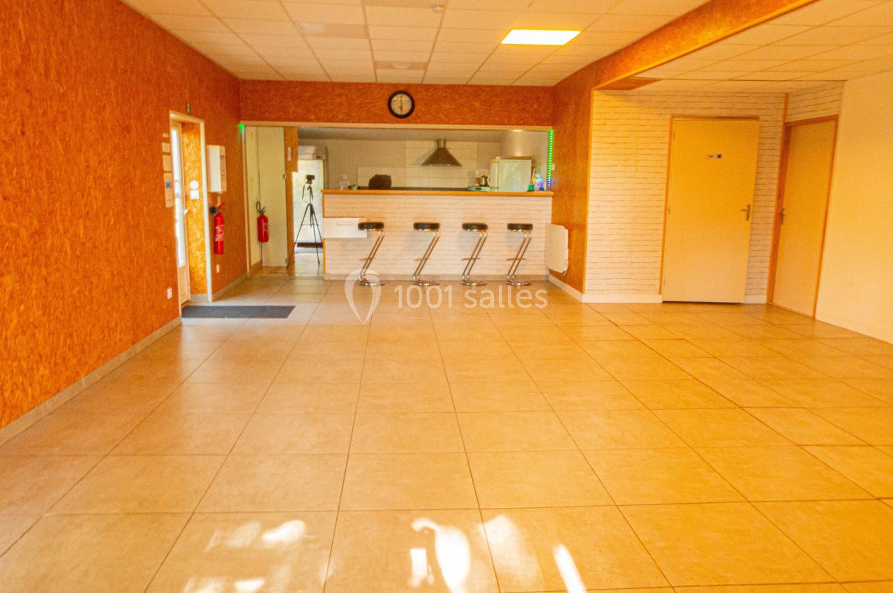 Salle lumineuse avec carrelage beige, comptoir avec tabourets hauts, murs en bois et briques, et plafond à dalles blanches.