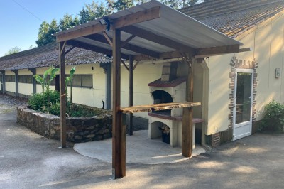 Chaise en bois marquée ’Gîte de la Barre’ dans un jardin verdoyant près d'une maison en pierre et crépi.