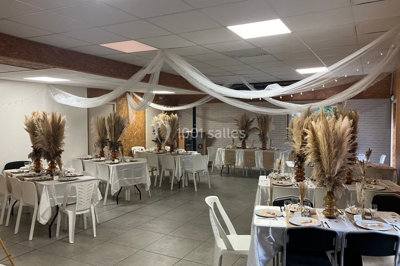 Salle décorée pour un événement avec des tables dressées, des nappes blanches et des compositions de pampas en centre de…