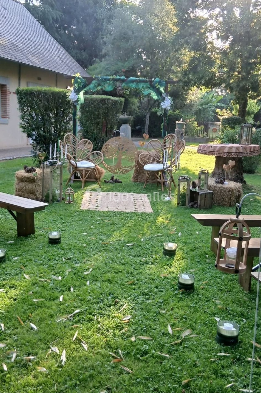 Espace extérieur aménagé pour une cérémonie, avec chaises en rotin, arche décorée et lanternes sur pelouse.