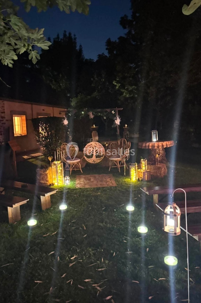 Espace extérieur nocturne décoré avec des lanternes, des guirlandes lumineuses et un mobilier de jardin en rotin.