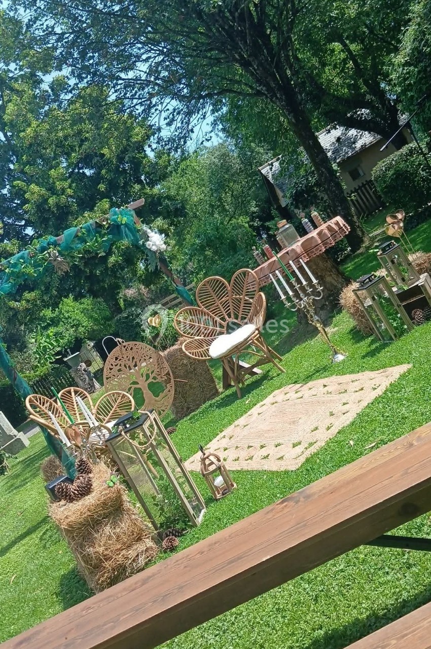 Décoration de mariage champêtre en extérieur avec arche fleurie, mobilier en rotin et bottes de foin sur pelouse.