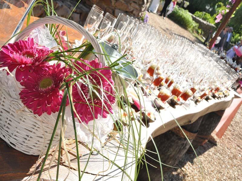 Panier de fleurs roses posé sur une table en bois avec des verres et des amuse-bouches alignés en extérieur.