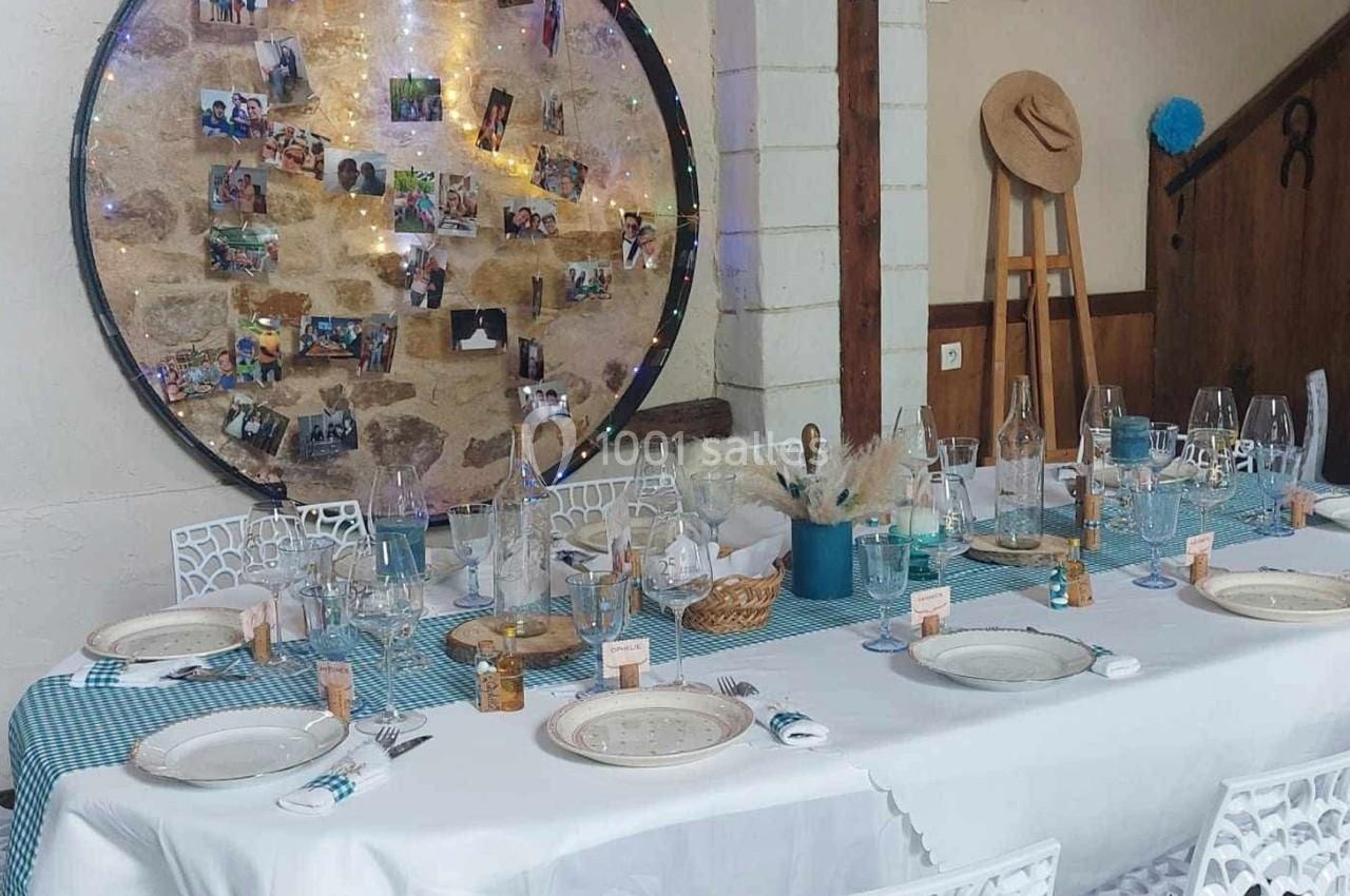 Table dressée pour un repas festif avec nappes bleues, décorations rustiques et un panneau de photos en arrière-plan.