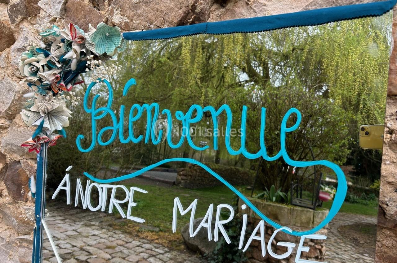 Texte ’Bienvenue à notre mariage’ écrit sur un miroir décoré de fleurs, reflétant un jardin verdoyant.