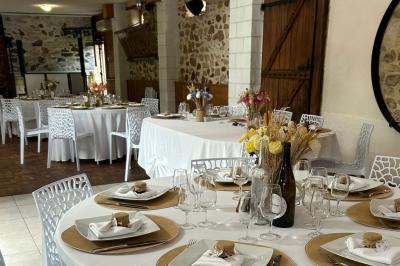 Salle de réception décorée avec des tables dressées, nappes blanches, chaises ajourées et compositions florales.