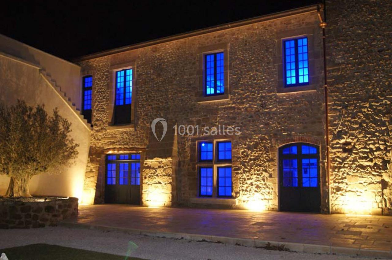 Façade en pierre d'un bâtiment éclairé par des lumières jaunes et bleues, de nuit.