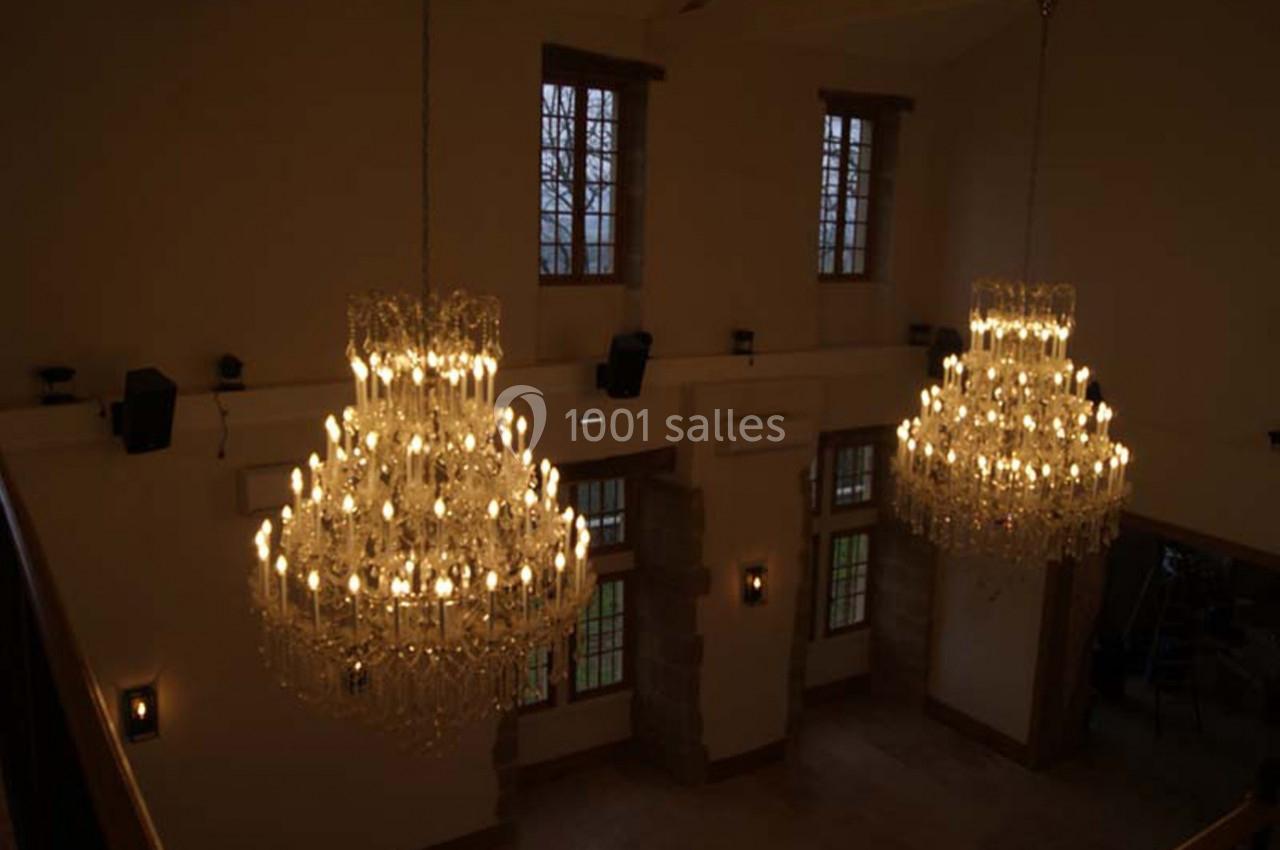 Deux grands lustres en cristal allumés suspendus dans une pièce avec de hautes fenêtres et des murs clairs.