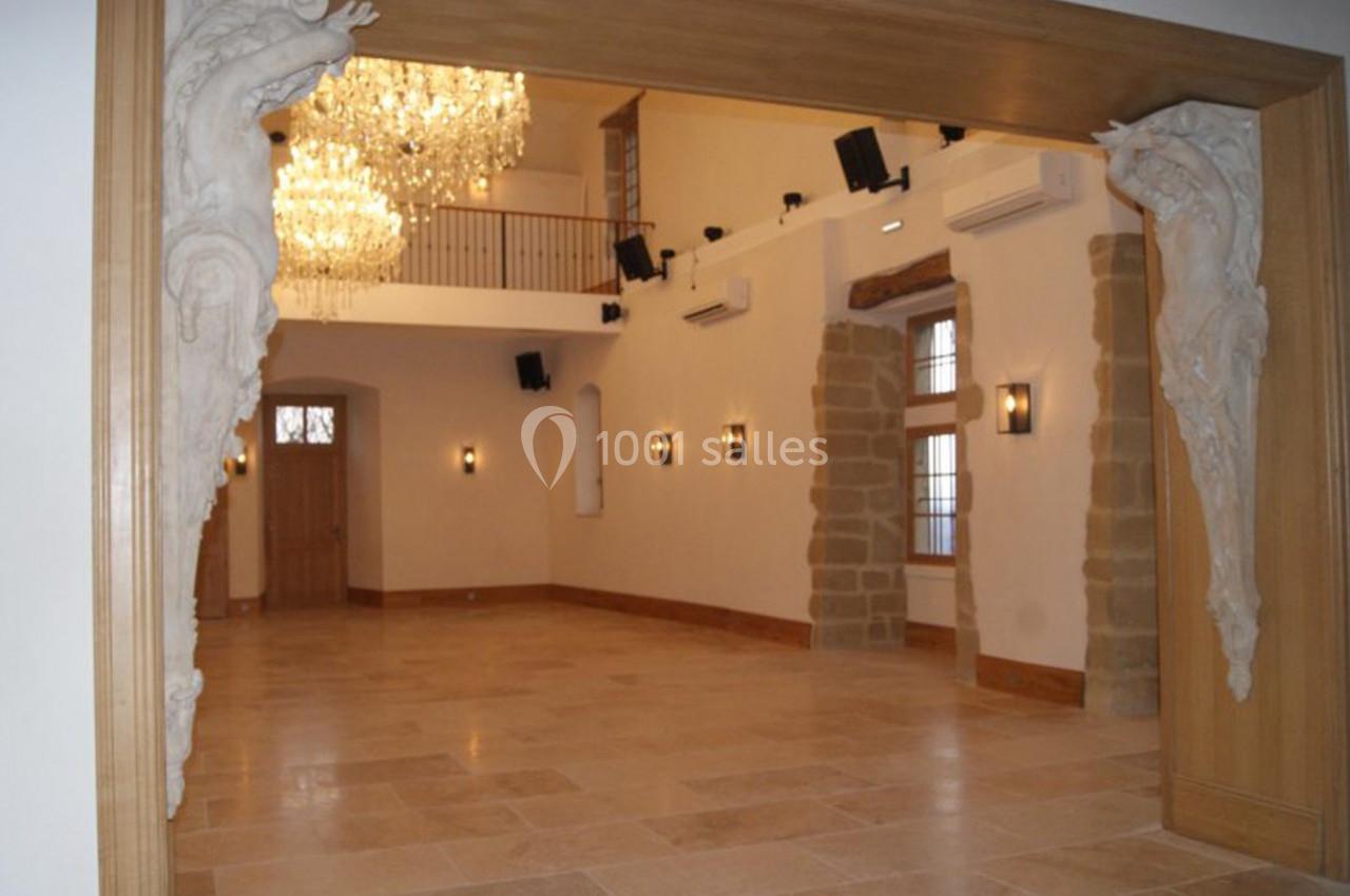 Salle lumineuse avec sol en pierre, lustre imposant, sculptures décoratives et murs ornés de fenêtres et appliques.