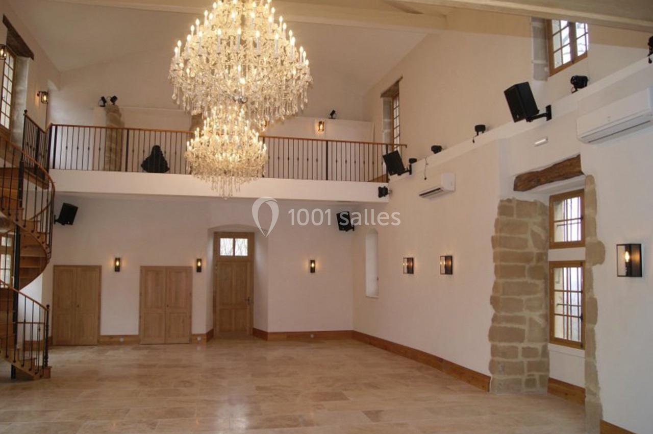 Salle spacieuse avec un sol en pierre, des lustres en cristal, des murs clairs et une mezzanine en bois.