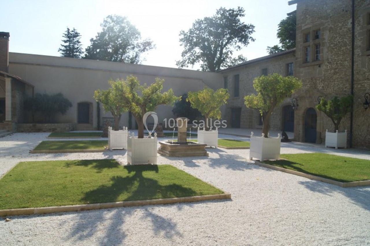 Cour intérieure avec fontaine centrale, arbres taillés, pelouses rectangulaires et bâtiments en pierre autour.