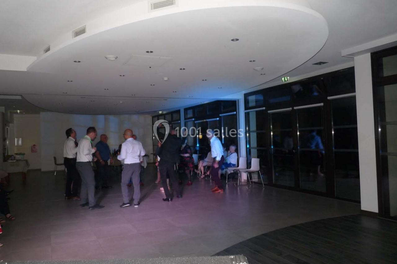 Des personnes dansent dans une salle moderne avec un éclairage tamisé et des baies vitrées en arrière-plan.