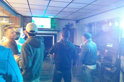 Un groupe de personnes chante au karaoké dans un bar éclairé par des lumières colorées.
