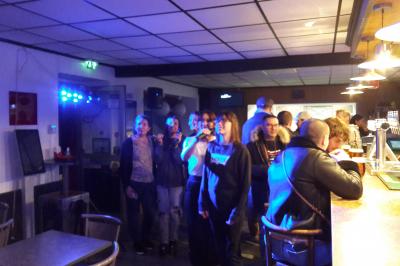 Un groupe de personnes chante au karaoké dans un bar éclairé par des lumières colorées.