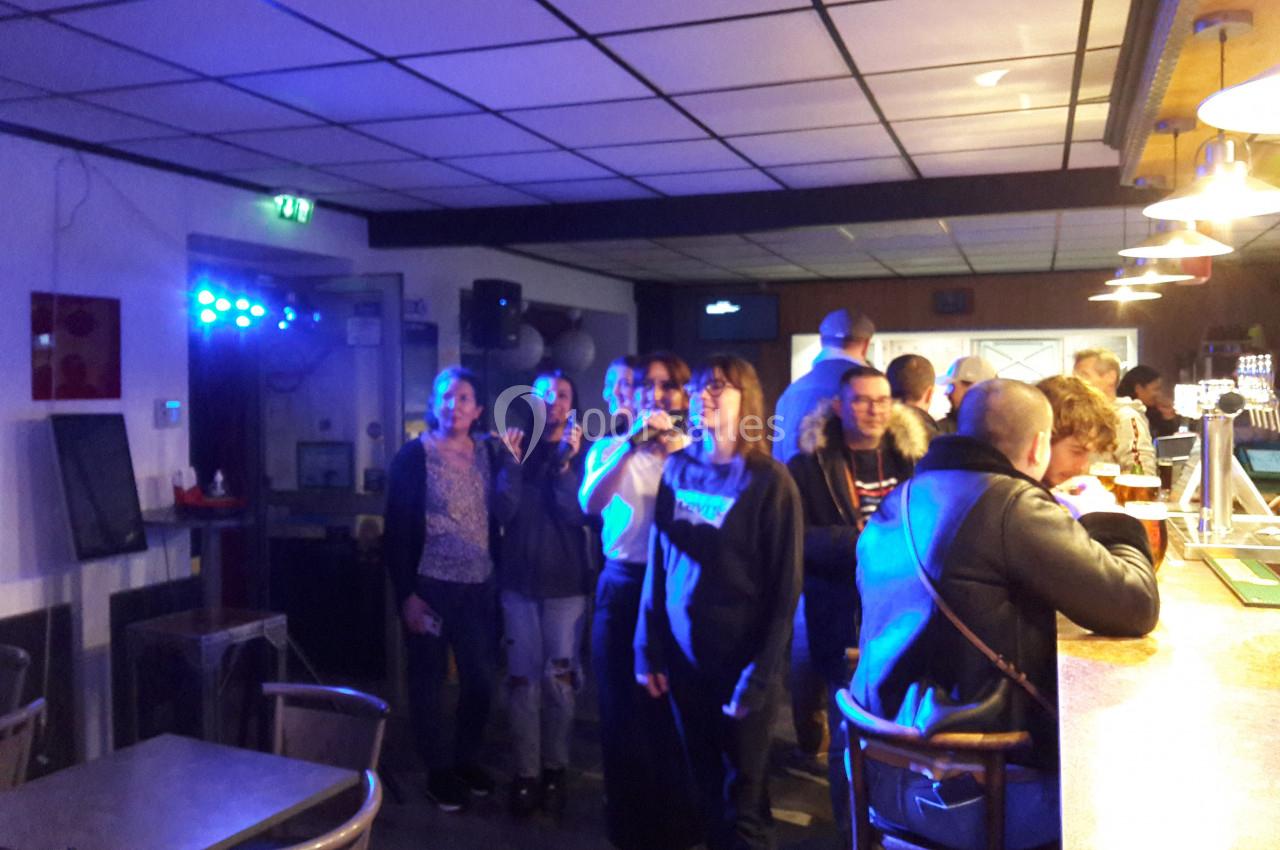Des personnes debout dans un bar, certaines sourient face à l'objectif, éclairées par une lumière bleutée.