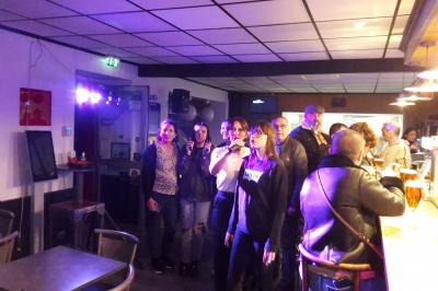 Un groupe de personnes chante au karaoké dans un bar éclairé par des lumières colorées.