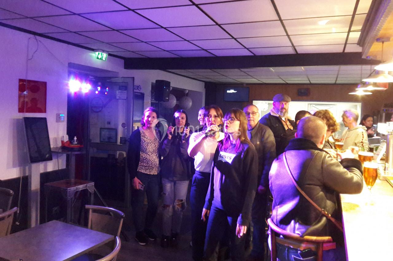 Un groupe de personnes chante au karaoké dans un bar éclairé par des lumières colorées.