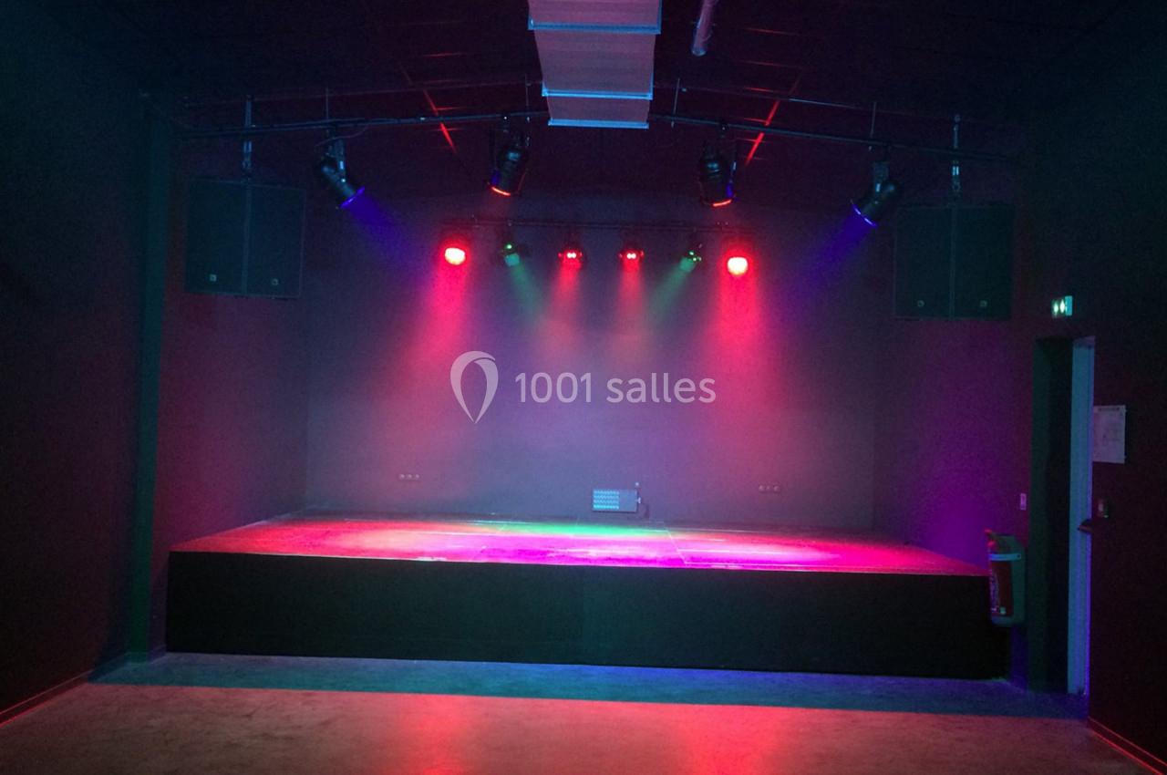 Scène vide éclairée par des projecteurs colorés dans une salle sombre avec un sol en béton.