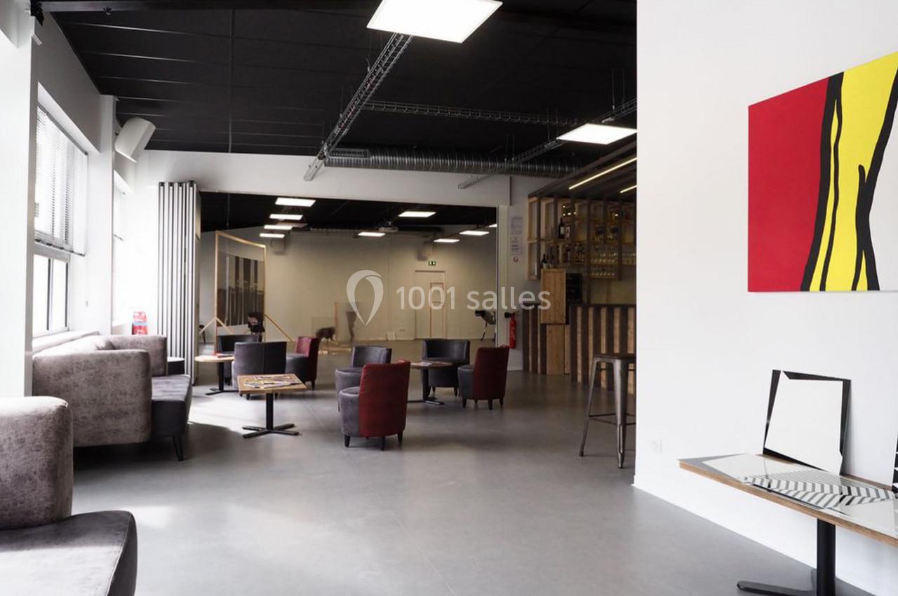 Espace intérieur lumineux avec mobilier varié, murs blancs, tableau coloré et plafond noir industriel.