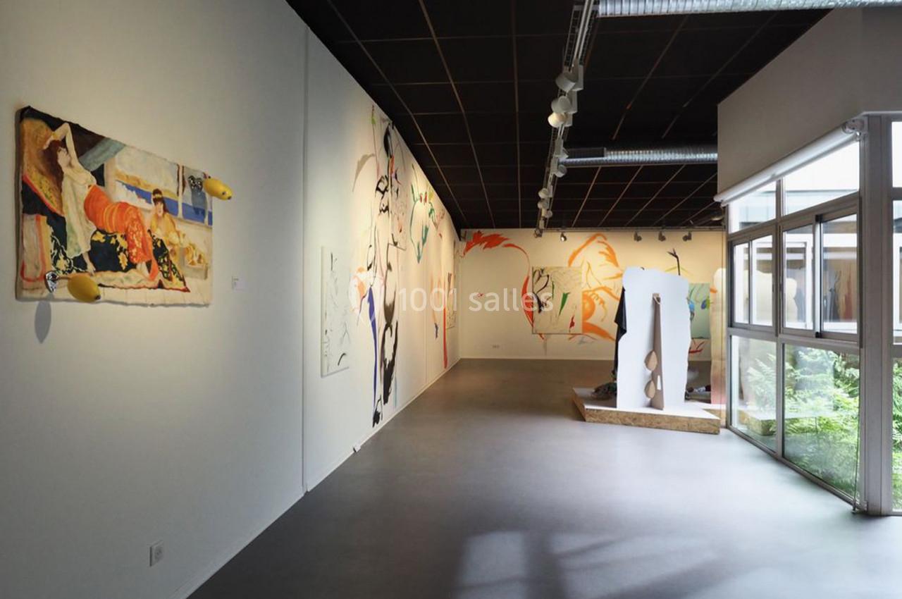 Vue d'une galerie d'art contemporaine avec des peintures murales colorées et des sculptures exposées près d'une baie vitrée.