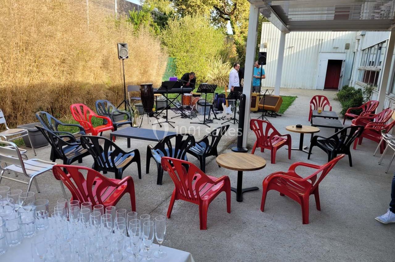 Chaises colorées disposées autour de petites tables sur une terrasse extérieure, avec instruments de musique en arrière-plan.
