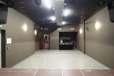 Salle vide avec sol en béton, murs sombres, éclairage au plafond et une table de mixage au fond.